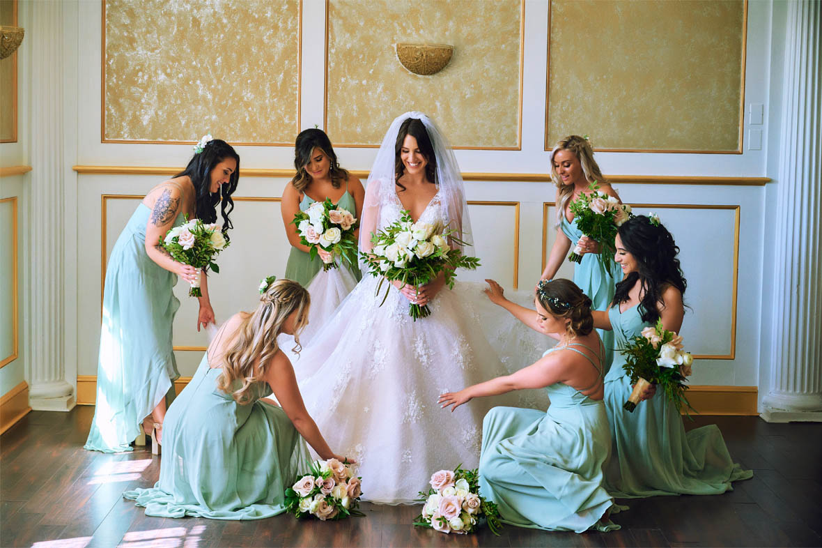 Bride holding flowers while bridesmaids fix the dress