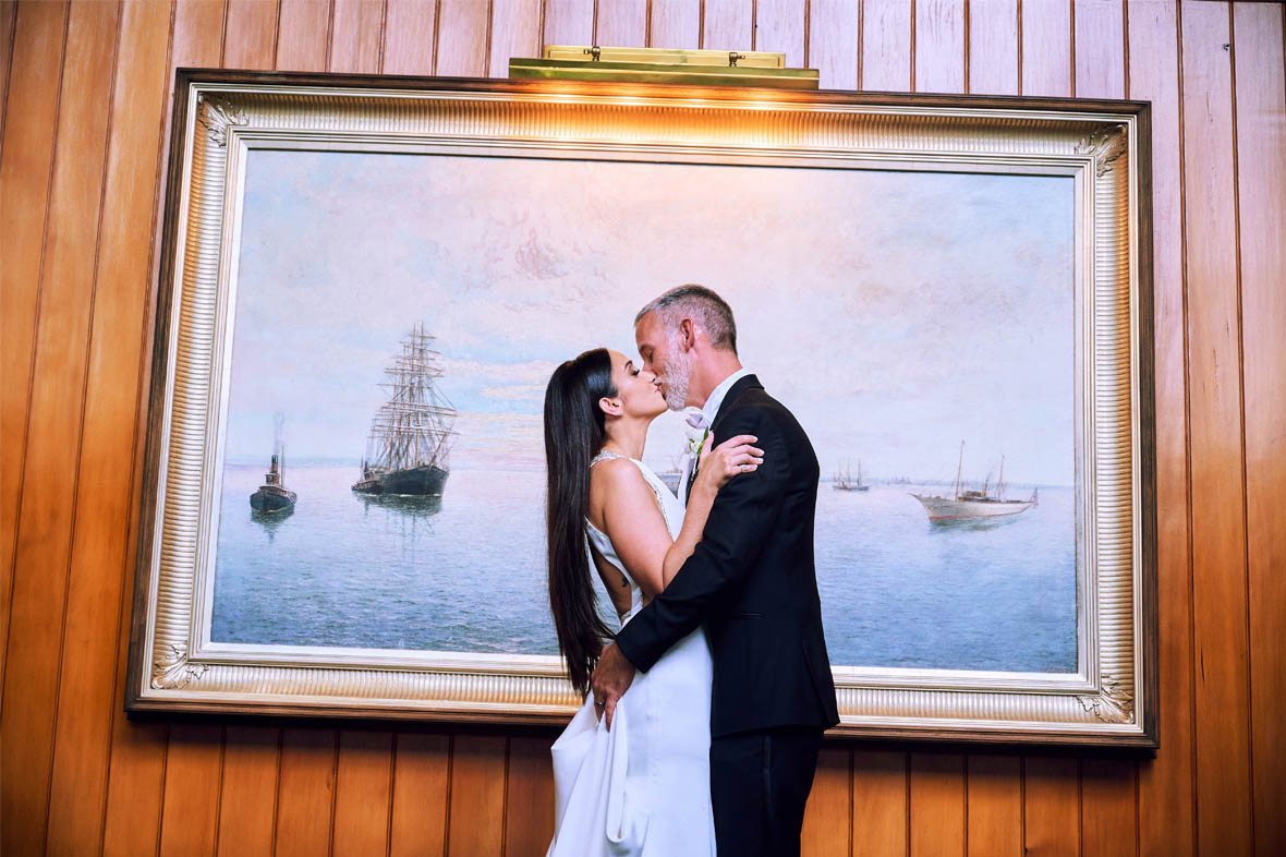 Bride and groom kissing in front of big painting