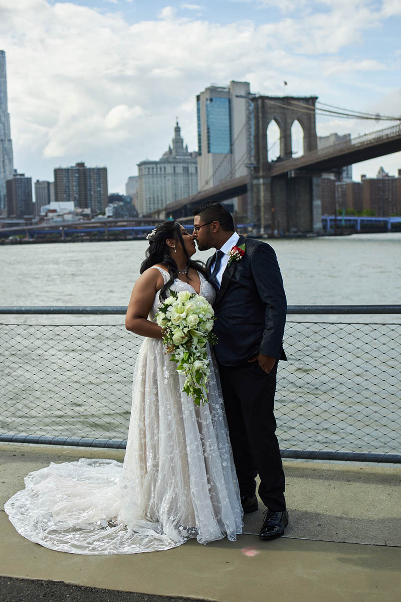 Bride and groom kissing in front of Brooklyn Bridge