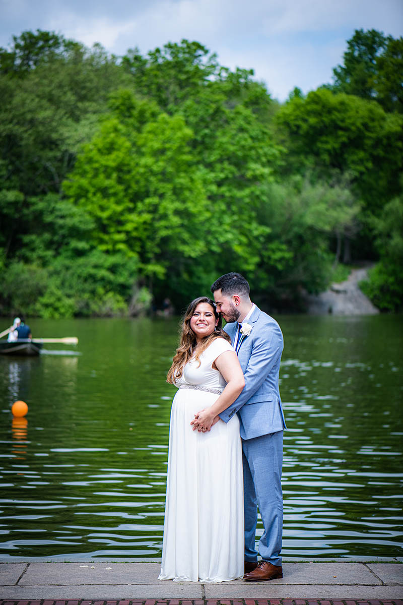 Groom hugging bride from behind by the water in Central Park