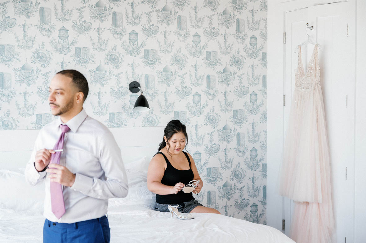 Groom fixing his tie and bride sitting on bed