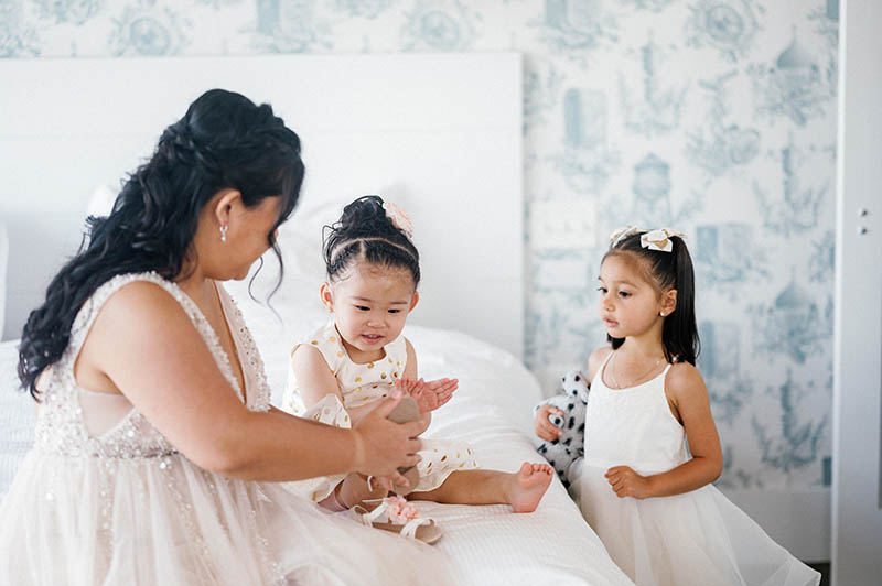 Bride playing with flower girls on bed