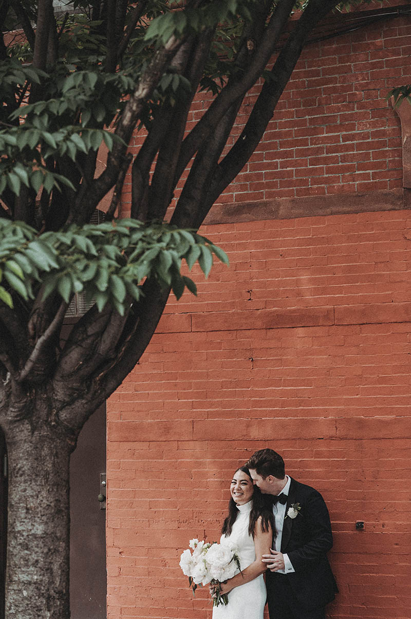 Groom kissing bride against brick wall