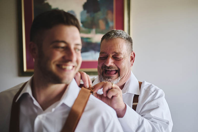 Father of the groom helping grooms brother get ready