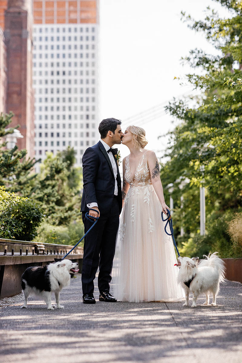 Bride and groom kissing while holding dogs on leash